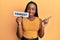 Young african american woman holding comedy word paper smiling happy pointing with hand and finger to the side