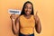 Young african american woman holding comedy word paper smiling happy and positive, thumb up doing excellent and approval sign