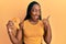 Young african american woman holding fourth place badge pointing thumb up to the side smiling happy with open mouth