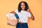 Young african american woman holding laundry basket smiling happy and positive, thumb up doing excellent and approval sign