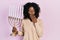 Young african american woman holding menorah hanukkah jewish candle covering mouth with hand, shocked and afraid for mistake