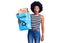 Young african american woman holding recycling bag with paper and cardboard scared and amazed with open mouth for surprise,