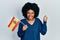 Young african american woman holding spain flag screaming proud, celebrating victory and success very excited with raised arm