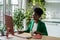 Young African American woman secretary working sits at office desk with computer and drinking coffee