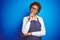 Young african american woman shop owner wearing business apron over blue background with hand on chin thinking about question,