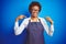 Young african american woman shop owner wearing business apron over blue background looking confident with smile on face, pointing