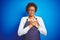 Young african american woman shop owner wearing business apron over blue background smiling with hands on chest with closed eyes