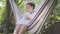 Young African American woman sitting in the hammock, relaxing in the garden, texting on her tablet. Leisure outdoors