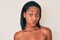 Young african american woman standing topless showing skin puffing cheeks with funny face