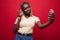 Young African American woman taking a selfie isolated on red background