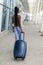 Young african american woman walking at airport walkway with suitcase, back view