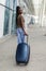 Young african american woman walking at airport walkway with suitcase, back view