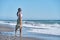 Young African American woman walking along the shore of the beach with sandals in hand