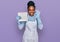 Young african american woman wearing apron washing dishes doing ok sign with fingers, smiling friendly gesturing excellent symbol