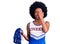 Young african american woman wearing cheerleader uniform holding pompom covering one eye with hand, confident smile on face and