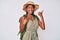 Young african american woman wearing explorer hat pointing thumb up to the side smiling happy with open mouth