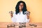 Young african american woman wearing optician uniform holding glasses sitting on the table smiling with a happy and cool smile on