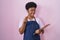 Young african american woman wearing professional waitress apron holding clipboard doing money gesture with hands, asking for