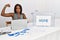 Young african american woman working at political election sitting by ballot strong person showing arm muscle, confident and proud