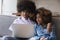 Young African couple sit on sofa using laptop