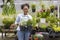 Young African customer is choosing rosemary and sage plant from the local garden center nursery with shopping cart full of summer