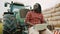 Young african farmer using tablet while sitting on green tractor. Haystack in the background