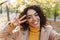 Young african happy woman walking outdoors in a spring park take a selfie by camera make peace gesture