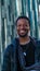 Young African man in a black outfit walking in a street posing in front of a glass paneled building