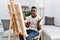 Young african man painting on canvas at home crazy and mad shouting and yelling with aggressive expression and arms raised