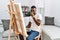 Young african man painting on canvas at home smelling something stinky and disgusting, intolerable smell, holding breath with