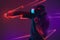 Young African man playing with VR set  on dark purple studio background in neon light with geometric luminescent