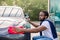 Young African man washing and wiping his modern blue gray car headlight at the outdoor car wash self service. Dark