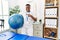 Young african physiotherapy man holding pilates ball at rehabilitation clinic smiling happy pointing with hand and finger