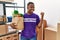 Young african volunteer man holding groceries pointing thumb up to the side smiling happy with open mouth