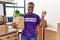 Young african volunteer man holding groceries smiling happy pointing with hand and finger to the side