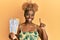 Young african woman with afro hair holding boarding pass smiling with an idea or question pointing finger with happy face, number