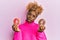 Young african woman with afro hair holding tasty colorful doughnuts in shock face, looking skeptical and sarcastic, surprised with