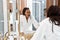 Young african woman anxiously looking at mirror reflection in bathroom