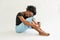 Young african woman hugs her knees sitting on the floor looking in camera in studio