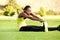 Young african woman sitting on grass stretching to reach toes