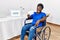 Young african woman sitting on wheelchair voting putting envelop in ballot box winking looking at the camera with sexy expression,