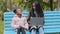 Young afro american mom with daughter on bench in city park friendly african family together looking in laptop outdoors