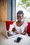 Young afro-american woman sitting behind laptop in cafe relaxing and drink milkshake