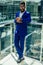 Young afro businessman in blue suit stands in office looks through big window at the city in airport terminal