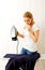 Young aghast woman standing behind ironing desk with iron in hand