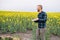 Young agronomist holds laptop in rape field. Agribusiness concept. agricultural engineer standing in a rape field with a laptop in