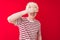 Young albino blond man wearing striped t-shirt and glasses over isolated red background smiling and laughing with hand on face