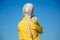 A young albino woman in yellow is standing with her back to the camera, a bunch of daisies on her shoulder. against the