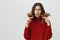 Young amazed stunned female model wearing red sweater looking with puzzlement and confusion at her dark long hair, being