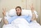 Young American man lying in bed at hospital room sick or ill but making victory sign with fingers smiling happy and positive